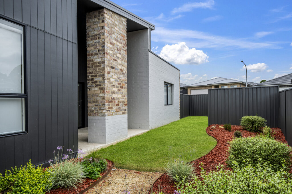Renovated home exterior with dark cladding, stone feature and landscaped garden