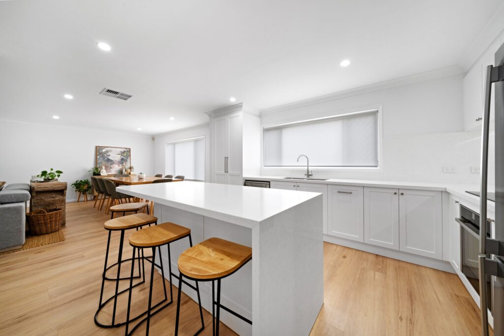 Renovated white kitchen with island bench and timber bar stools in Lidcombe by Daylo Build