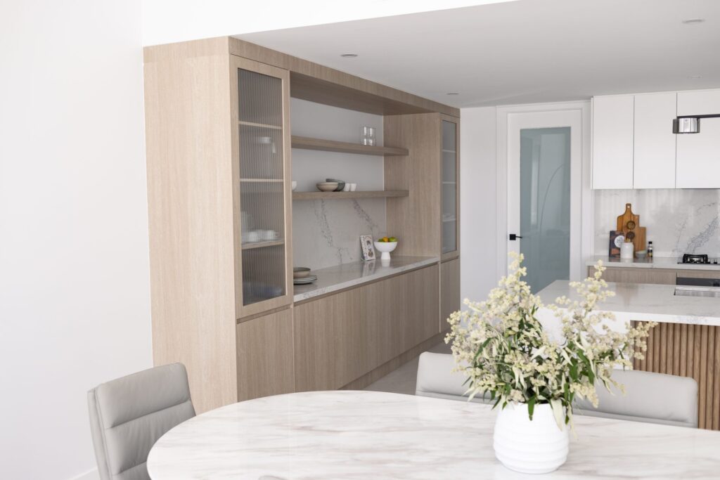 Custom timber kitchen joinery with glass-front cabinets and stone splashback beside the dining table in a Box Hill home