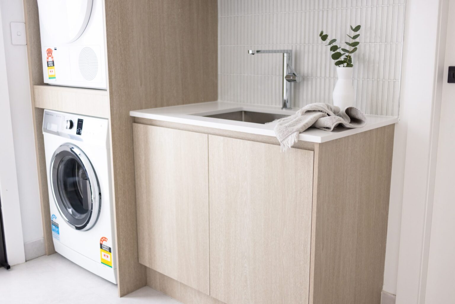 Renovated laundry with stacked washer and dryer, custom timber cabinetry, benchtop and sink in Box Hill by Daylo Build