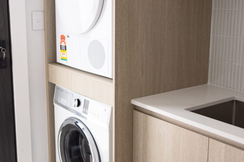 Custom laundry joinery with tall storage, stacked washer and dryer and tiled splashback