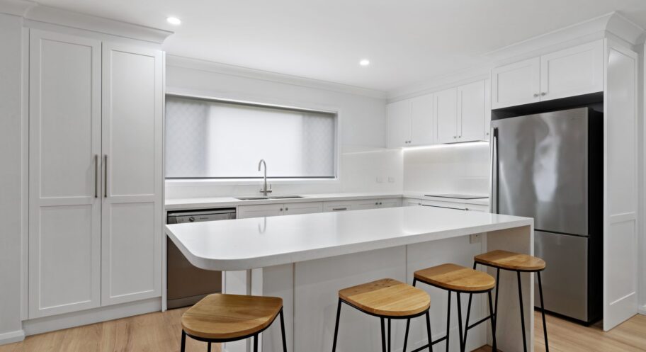 White shaker kitchen with island, Lidcombe White shaker-style kitchen with island bench and bar stools in a Lidcombe home renovation by Daylo Build